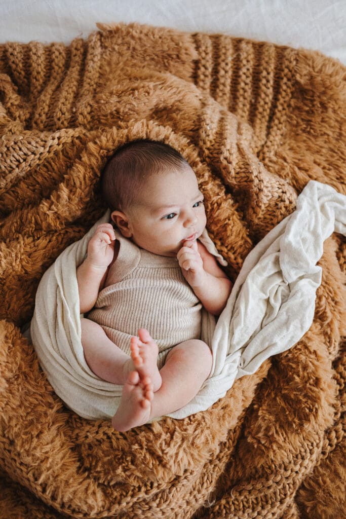 Newborn baby lying on bed during in home photo session